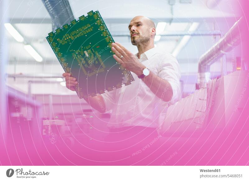 Confident mature male technician analyzing large circuit board in illuminated factory color image colour image indoors indoor shot indoor shots interior