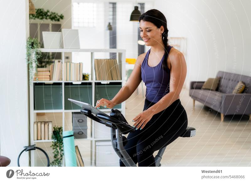 Young woman using digital tablet while sitting on exercise bike at home color image colour image indoors indoor shot indoor shots interior interior view