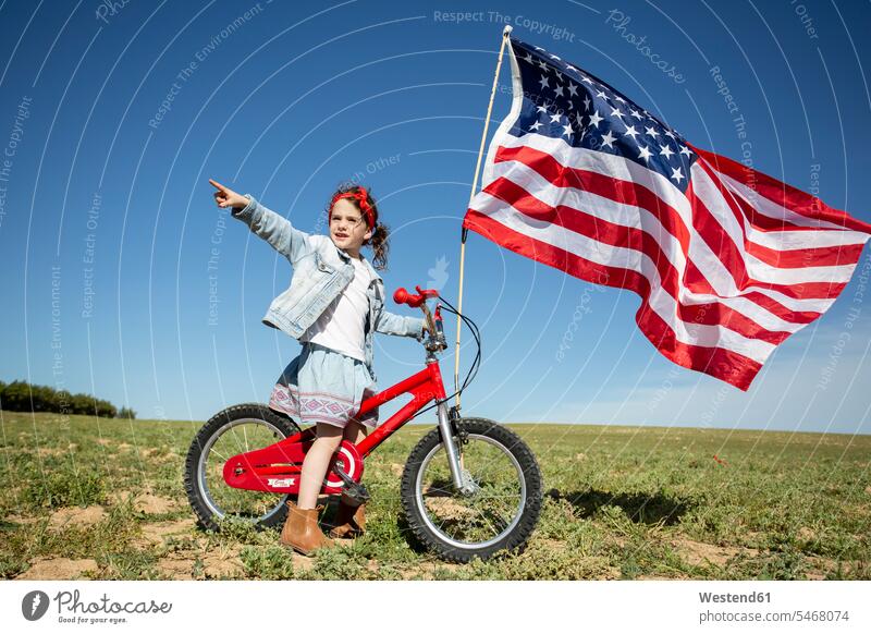 Girl with bicycle and American flag on field in remote landscape Field Fields farmland landscapes scenery terrain american girl females girls flags banner