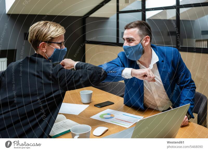 Male and female entrepreneurs wearing masks while greeting with elbow bump in board room during coronavirus pandemic color image colour image Businessman