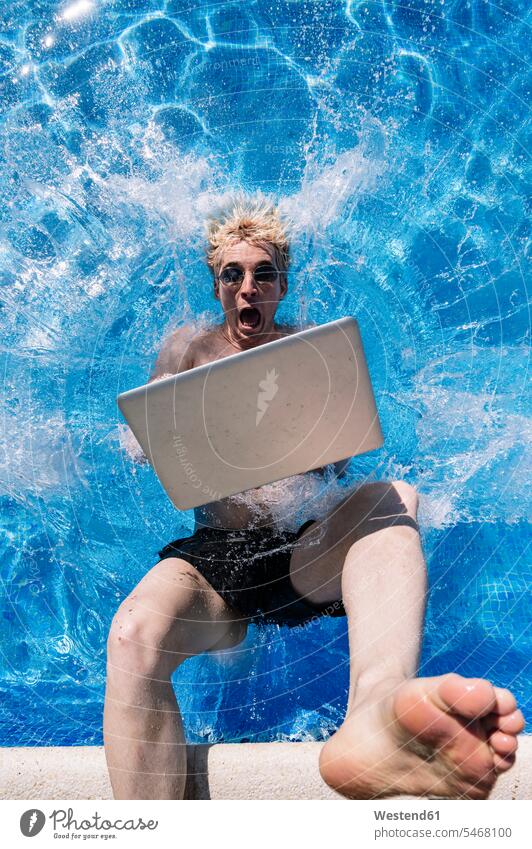Shocked young man with laptop falling in swimming pool color image colour image Spain leisure activity leisure activities free time leisure time outdoors