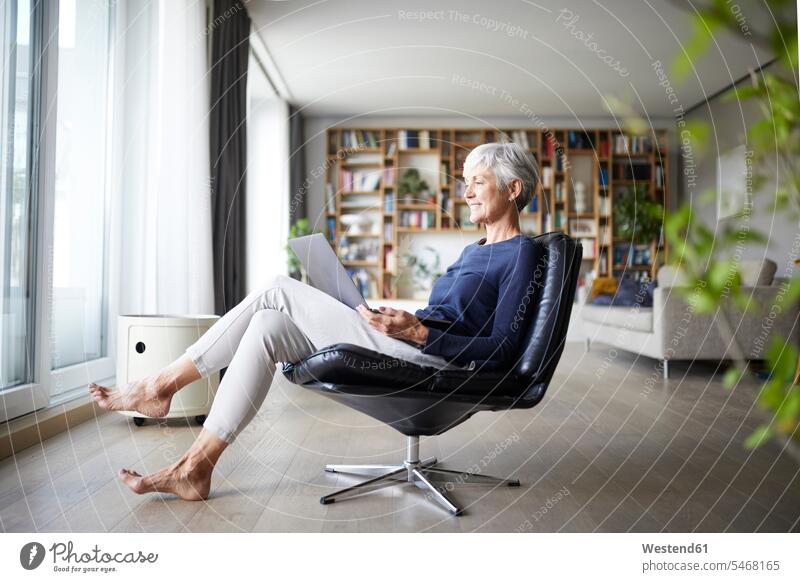 Active senior woman using laptop while sitting on chair at home color image colour image indoors indoor shot indoor shots interior interior view Interiors day