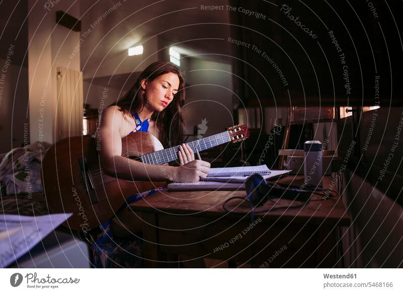Young woman writing in book while practicing guitar at home color image colour image domestic life domestic scene indoors indoor shot indoor shots interior