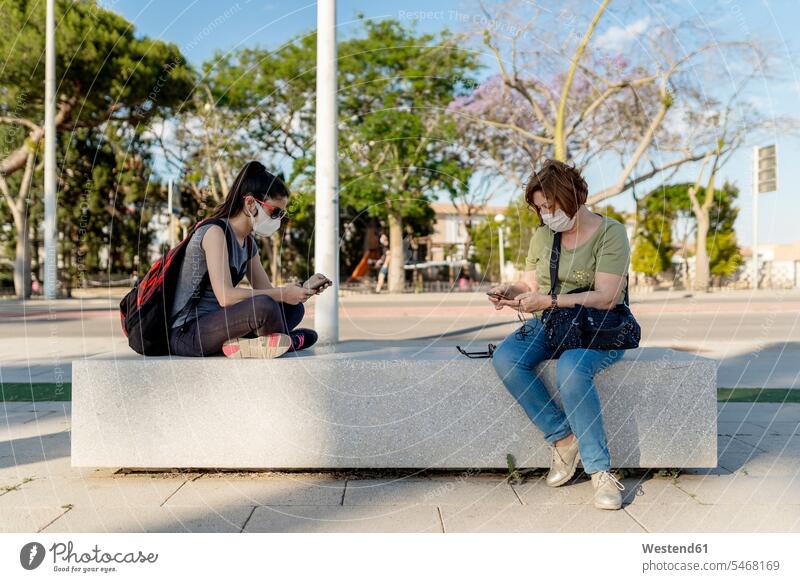 Women wearing masks using smart phones while sitting on seat in park color image colour image Spain leisure activity leisure activities free time leisure time