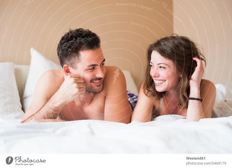 Happy young couple looking at each other while lying in bed at home color image colour image indoors indoor shot indoor shots interior interior view Interiors