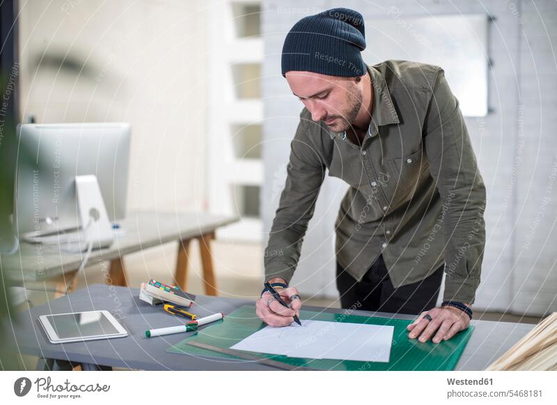 Young man taking notes at desk in office offices office room office rooms men males making a note note taking desks workplace work place place of work Adults