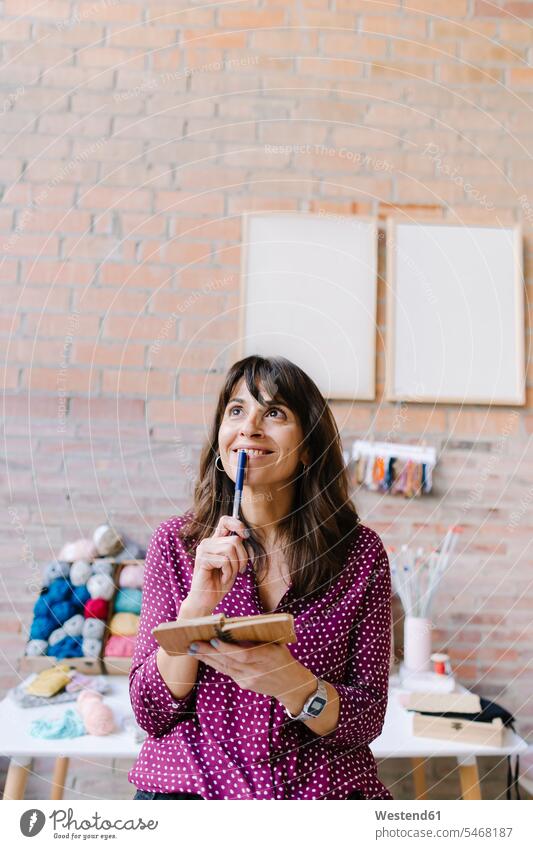 Smiling woman in knitting studio thinking and taking notes smiling smile making a note note taking females women studios Adults grown-ups grownups adult people