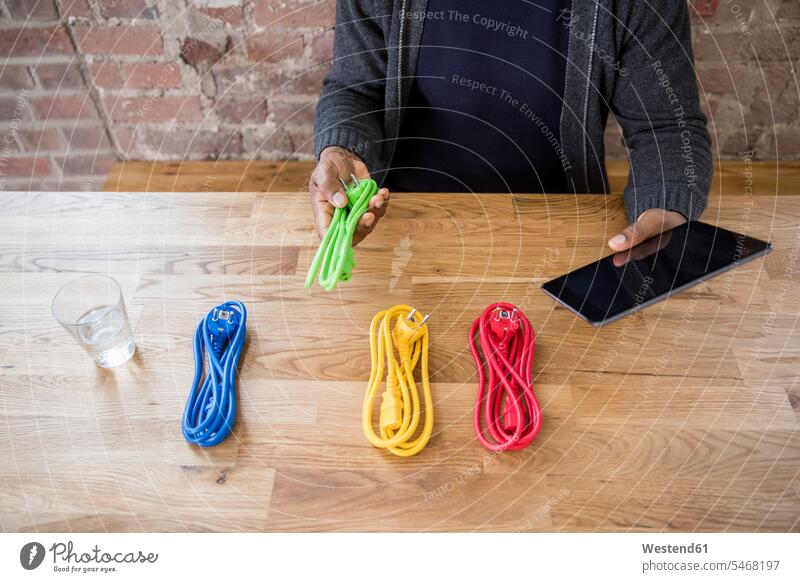 Businessman with tablet choosing from coloured power cables on table top, partial view power cord tabletop colored Business man Businessmen Business men colours