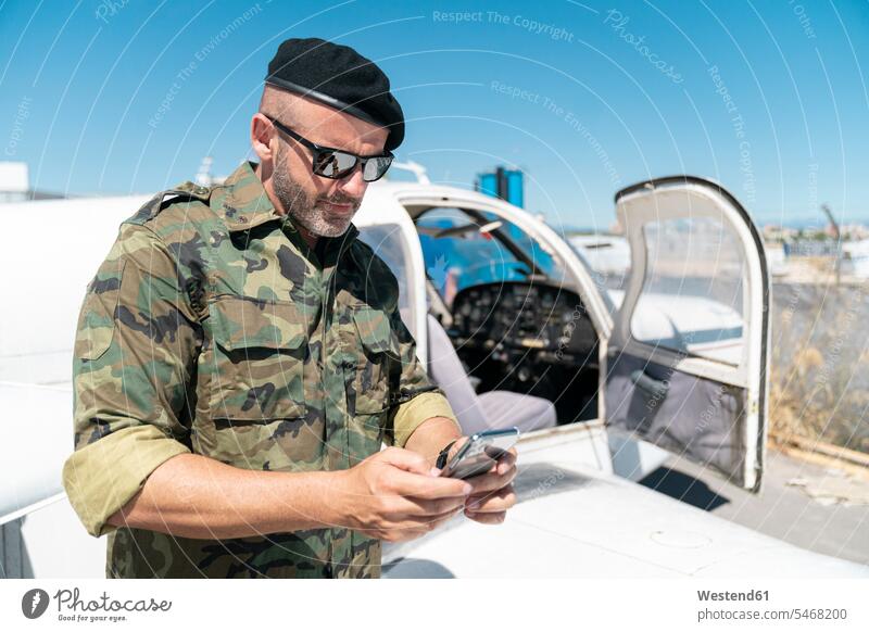 Army Soldier text messaging on smart phone during sunny day color image colour image outdoors location shots outdoor shot outdoor shots daylight shot