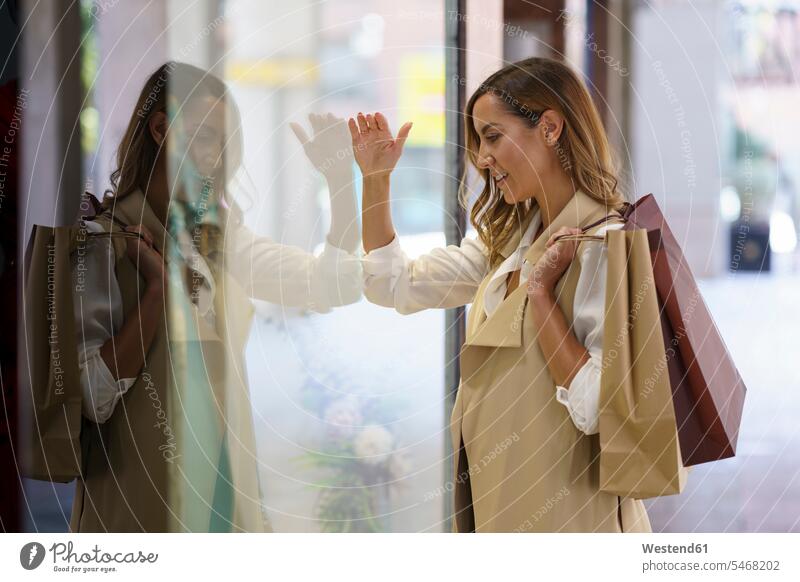 Woman with shopping bag standing while looking at shop window in city color image colour image outdoors location shots outdoor shot outdoor shots day