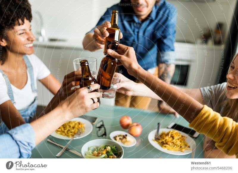 Cheerful friends clinking beer bottles at dining table Beer Beers Ale toasting cheers cheerful gaiety Joyous glad Cheerfulness exhilaration merry gay