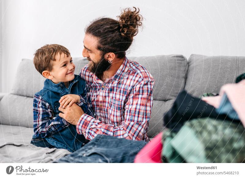 Father and son sitting together on the couch folding laundry father pa fathers daddy papa settee sofa sofas couches settees Seated Laundry parents family