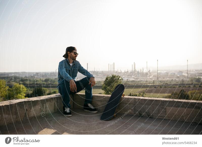 Skateboarder dressed in casual clothes resting at sunset recreation relaxing Recreational jeans Denim Jeans sitting Seated city town cities towns man men males