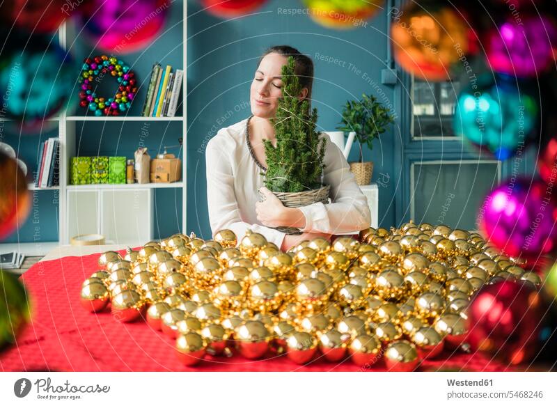 Woman sitting at table with many golden Christmas baubles holding potted fir tree woman females women Fir Trees Gold Color Gold Colored christmas bauble