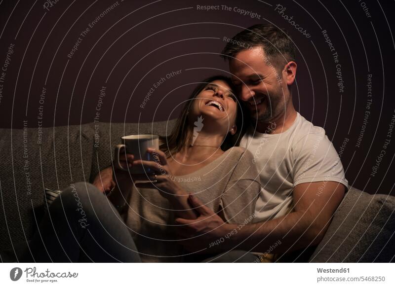 Loving couple laughing while relaxing on sofa against wall at home color image colour image Spain indoors indoor shot indoor shots interior interior view