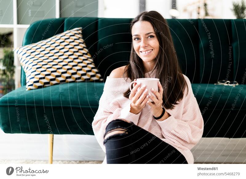 Smiling woman sitting with coffee cup against sofa at home color image colour image indoors indoor shot indoor shots interior interior view Interiors