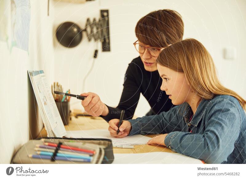 Mother helping daughter doing homework at home Tables desks pencil pencils pens learn write Seated sit speak speaking talk Lifestyle conversation conversations