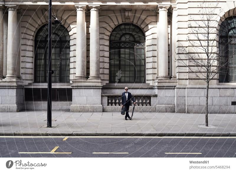 UK, London, stylish senior businessman with briefcase and umbrella standing on pavement Businessman Business man Businessmen Business men brief case senior men