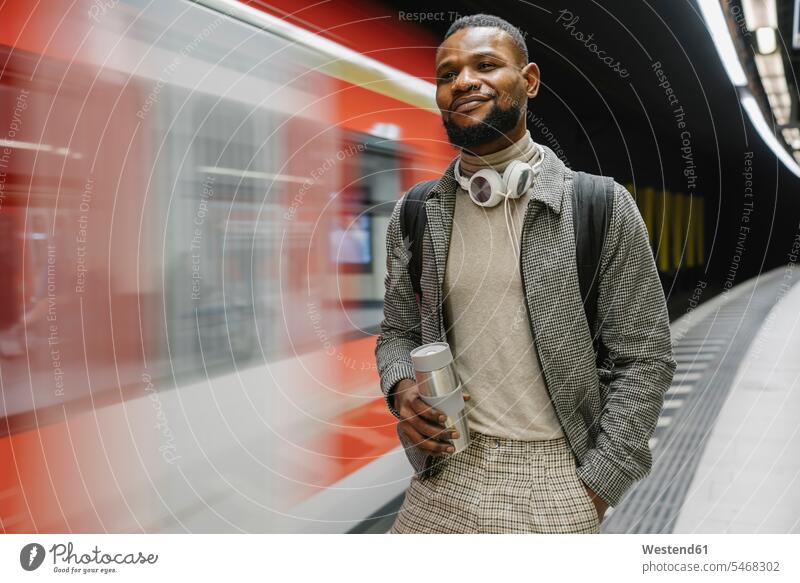 Stylish man with reusable cup and headphones in a metro station touristic tourists business life business world business person businesspeople Business man