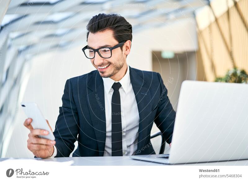 Smiling businessman looking at cell phone at desk in modern office Businessman Business man Businessmen Business men smiling smile offices office room