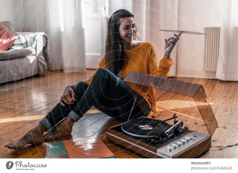 Smiling young woman sitting on the floor at home with record and record player human human being human beings humans person persons Mixed Race