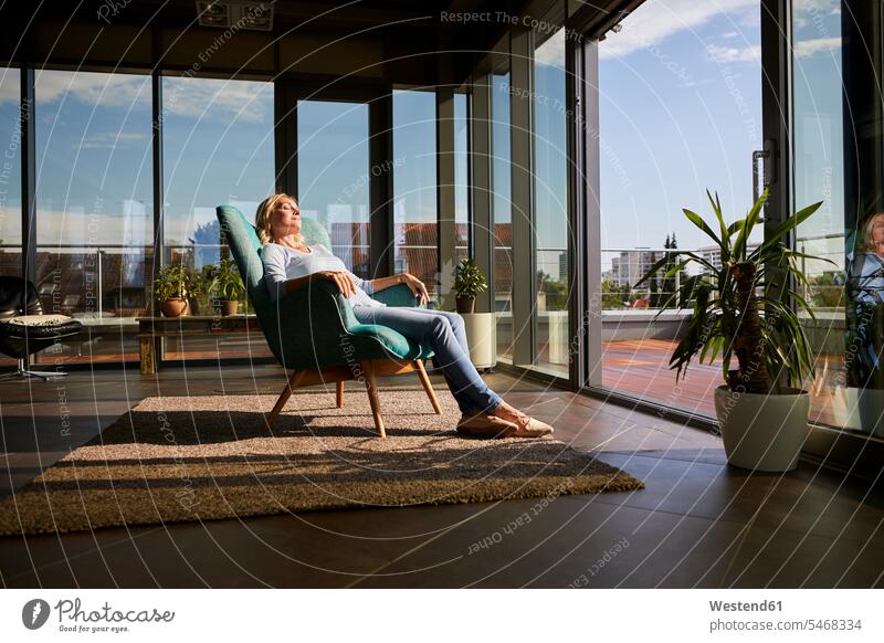 Mature woman relaxing in armchair in sunlight at home females women Arm Chairs armchairs Sunlit relaxed relaxation Adults grown-ups grownups adult people
