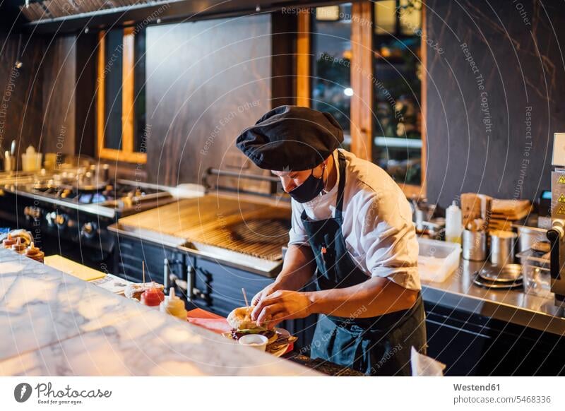 Chef wearing protective face mask preparing burgers in restaurant kitchen human human being human beings humans person persons 1 one person only only one person