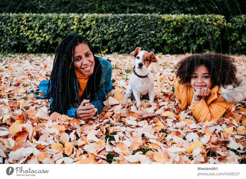 Smiling woman and daughter lying on dry leaf by dog sitting at park color image colour image outdoors location shots outdoor shot outdoor shots day