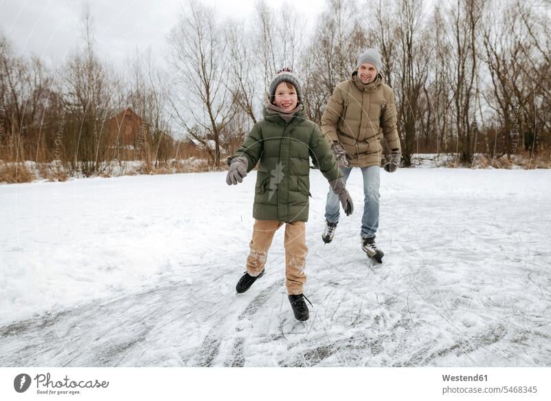 Happy boy skating together with father on ice covered in snow snow covered snow topped snow-topped snowy seasons hibernal Winter Clothes Winter Clothing