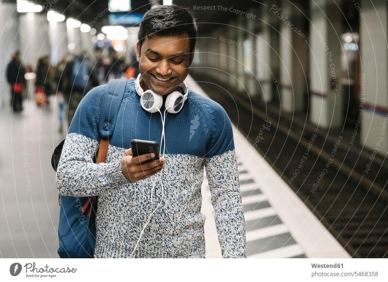 Smiling man using smartphone in subway station touristic tourists back-pack back-packs backpacks rucksack rucksacks jumper sweater Sweaters transport railroad