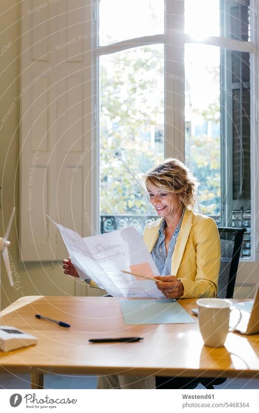 Smiling female engineer examining blueprint while sitting in office color image colour image indoors indoor shot indoor shots interior interior view Interiors