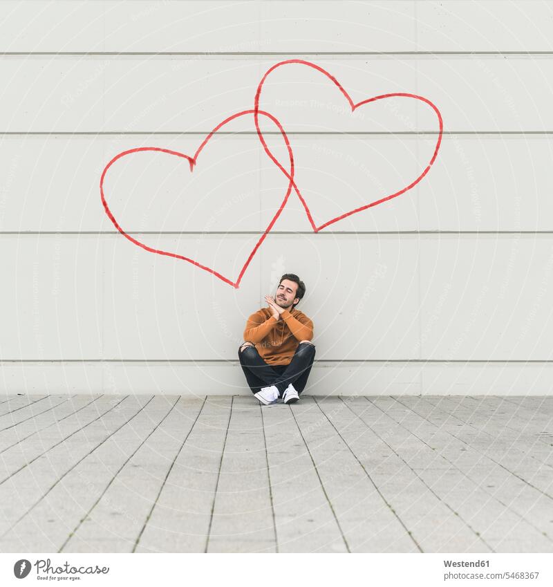 Digital composite of young man sitting at a wall with hearts human human being human beings humans person persons celibate celibates singles solitary people