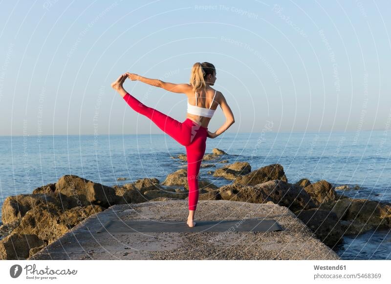 Young woman practicing yoga on the beach, doing standing balance, Utthita Hasta Padangustasana balanced Equilibrium exercise exercising practice practise