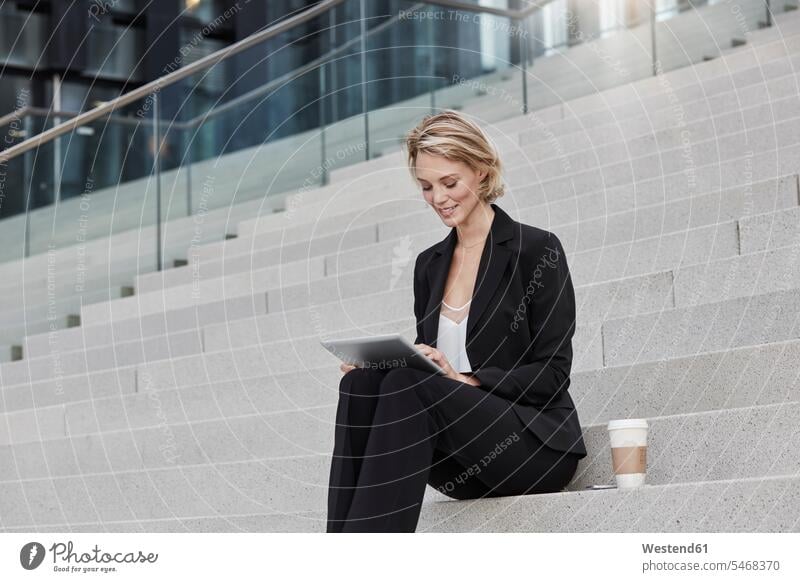 Blond businesswoman with coffee to goe sitting on stairs using tablet businesswomen business woman business women digitizer Tablet Computer Tablet PC