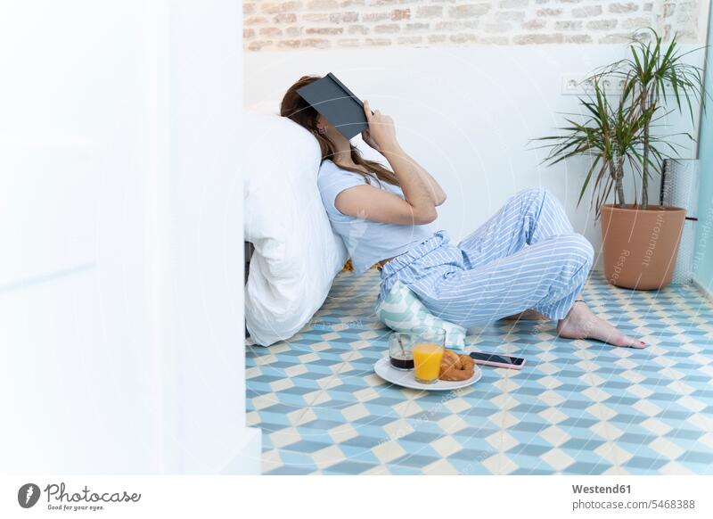 Young woman sitting on the floor and a book on her head in bedroom human human being human beings humans person persons caucasian appearance caucasian ethnicity