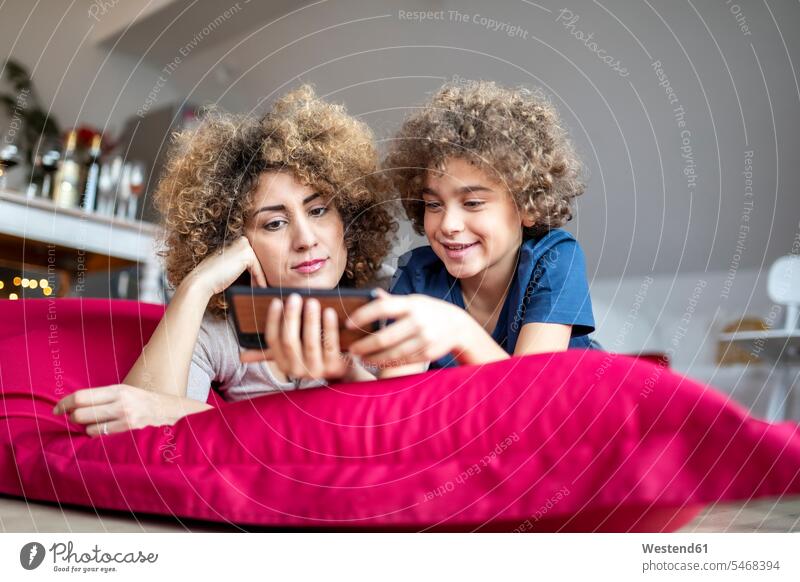 Mother and son watching a video on smartphone, lying on big pillow human human being human beings humans person persons caucasian appearance caucasian ethnicity