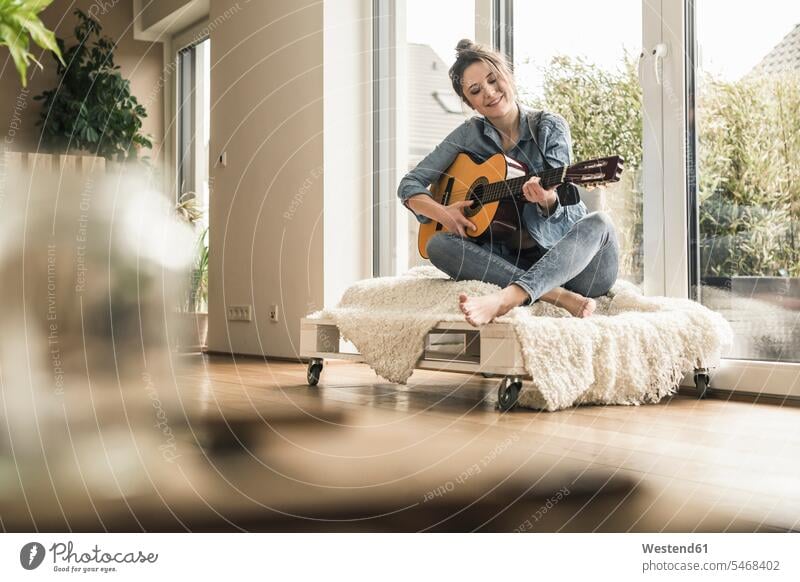 Smiling woman sitting at the window at home playing guitar females women guitars windows smiling smile Seated Adults grown-ups grownups adult people persons