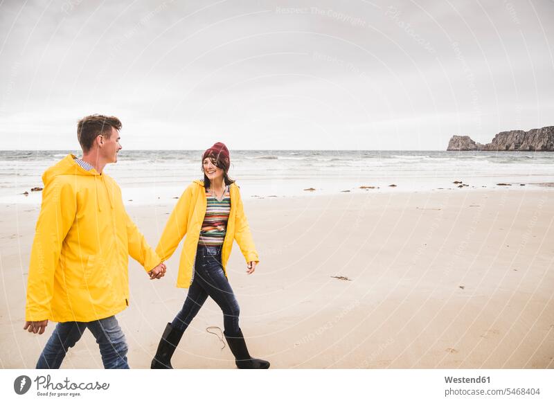 Young woman wearing yellow rain jackets and walking along the beach, Bretagne, France human human being human beings humans person persons caucasian appearance