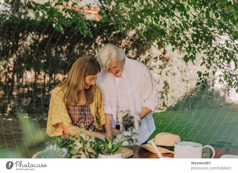 Mother and daughter playing with dog by table in yard color image colour image Spain leisure activity leisure activities free time leisure time casual clothing