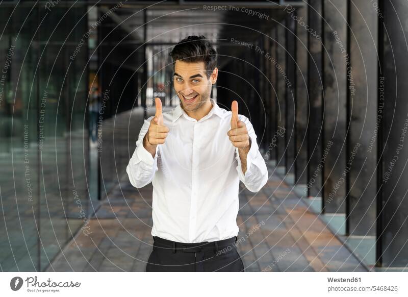 Smiling businessman showing thumbs up while standing in office color image colour image Spain day daylight shot daylight shots day shots daytime Businessman