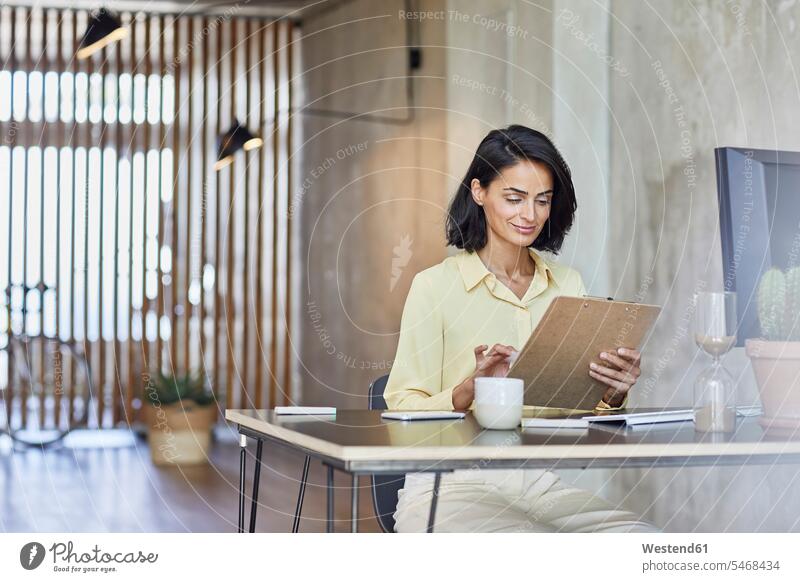Businesswoman holding clipboard while working at desk in office color image colour image Germany indoors indoor shot indoor shots interior interior view