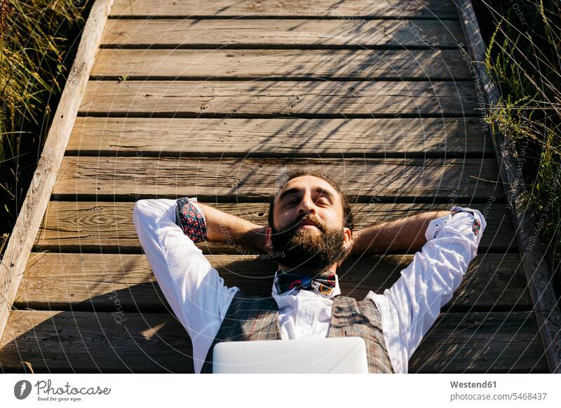 Well dressed man with laptop lying on a wooden walkway in the countryside human human being human beings humans person persons caucasian appearance