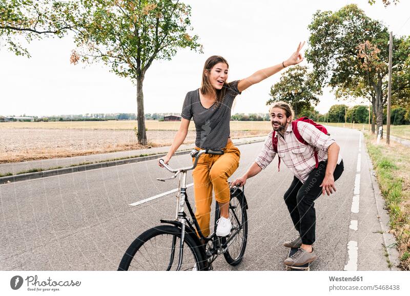 Happy young couple with bicycle and skateboard on country road bikes bicycles rural road rural roads country roads happiness happy twosomes partnership couples