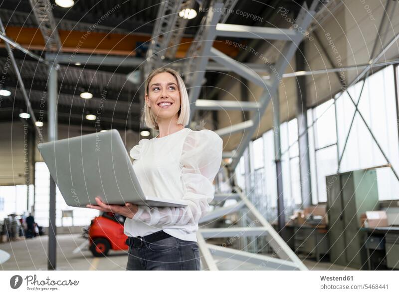 Smiling young woman using laptop in a factory human human being human beings humans person persons caucasian appearance caucasian ethnicity european 1