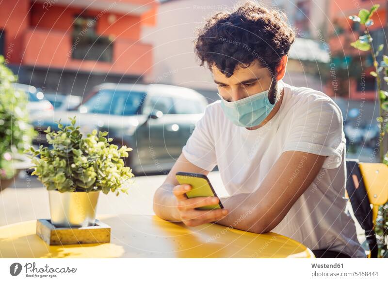 Young man wearing face mask using smart phone while sitting at sidewalk cafe color image colour image leisure activity leisure activities free time leisure time