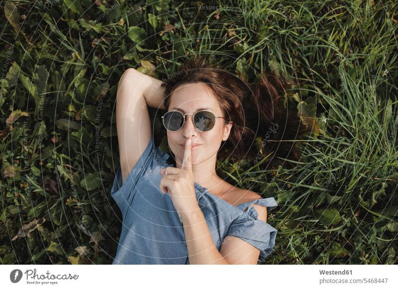Portrait of smiling woman wearing sunglasses lying in grass laying down lie lying down sun glasses Pair Of Sunglasses females women smile portrait portraits