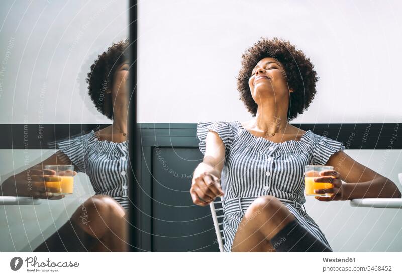 Relaxed woman holding glass of orange juice while sitting on chair at balcony in penthouse color image colour image indoors indoor shot indoor shots interior