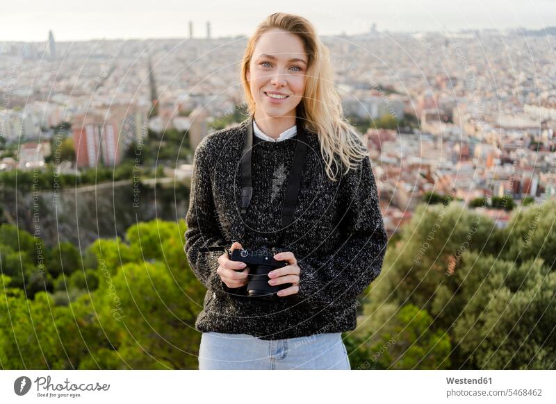 Portrait of smiling young woman with camera at sunrise above the city, Barcelona, Spain human human being human beings humans person persons