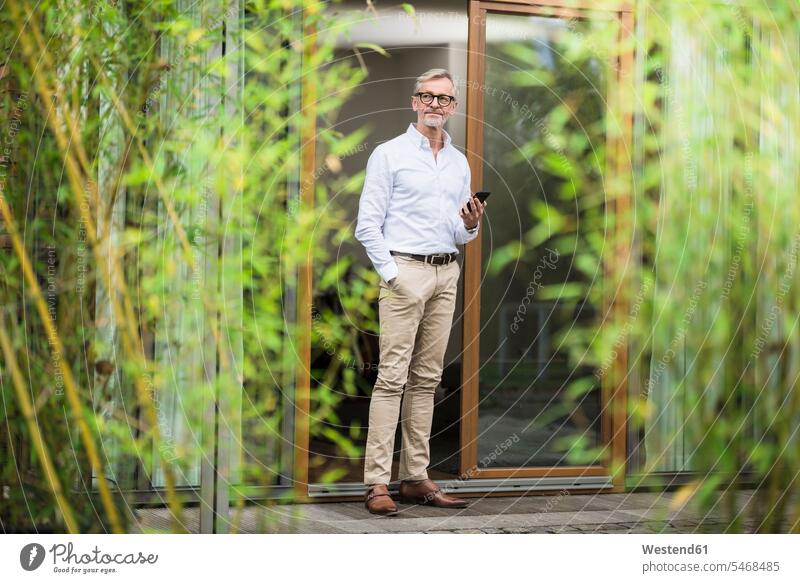 Senior man with grey hair standing in front of his modern design home holding smartphone human human being human beings humans person persons