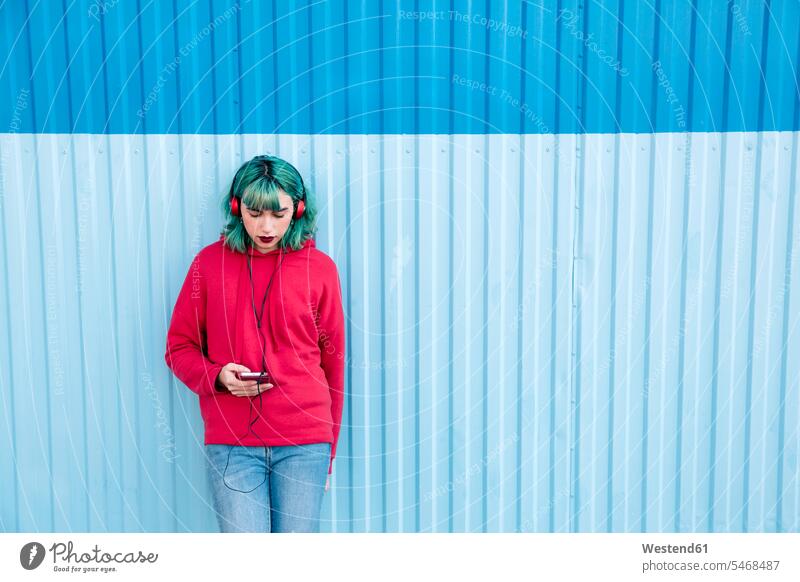 Young woman with blue dyed hair listening music with headphones while looking at smartphone portrait portraits females women Smartphone iPhone Smartphones view